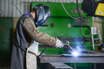 Fototapeta handsome man workshop welding iron spark fire hot steel with power GMAW welder and protective gear obraz