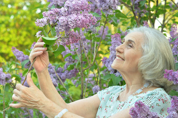 Portrait of happy senior beautiful woman with lilacs in spring park