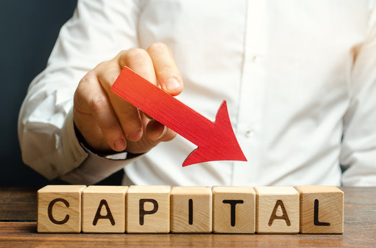 Wooden blocks with the word Capital and arrow down in the hands of a businessman. The concept of the fall in the level of authorized capital. Economic recession and crisis. Drop in return on equity