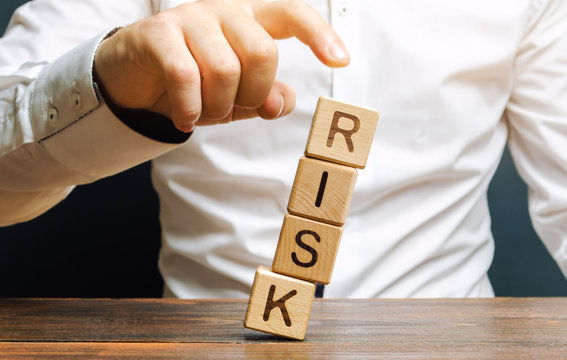 Man Removes Blocks With The Word Risk. The Concept Of Reducing Possible Risks. Insurance, Stability Support. Legal Protection Of Business Interests. Financial Pillow. Favorable Investment Climate.