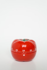 Close up view of mechanical tomato shaped kitchen clock timer for cooking & studying. Used for pomodoro technique for time and productivity management. Isolated on white background, set at 25 minutes.