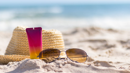 A bottle of sunscreen with sunglasses and panama hat  on a beach, summer skin remedies and protection, vacation at a sea