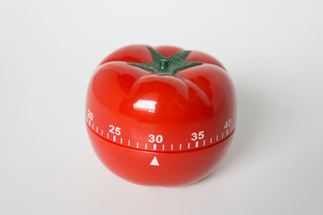 Close up view of mechanical tomato shaped kitchen clock timer for cooking & studying. Used for pomodoro technique for time and productivity management. Isolated on white background, set at 30 minutes.