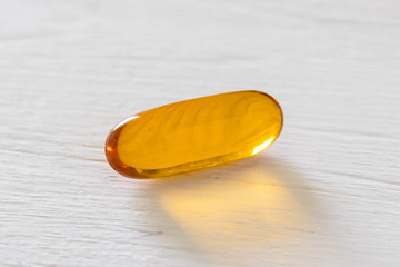 Close up view of fish oil capsule on white wooden background, vitamin and supplementa pill concept