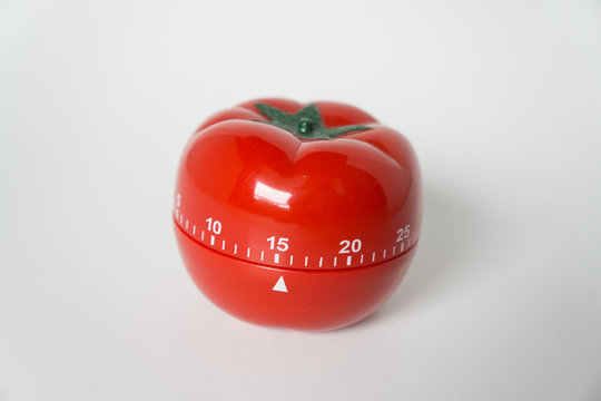 Close up view of mechanical tomato shaped kitchen clock timer for cooking & studying. Used for pomodoro technique for time and productivity management. Isolated on white background, set at 15 minutes.