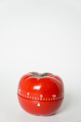 Close up view of mechanical tomato shaped kitchen clock timer for cooking & studying. Used for pomodoro technique for time and productivity management. Isolated on white background, set at 5 minutes.