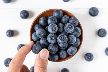 Blueberries in a wooden bowl on white table in top view or flat lay, eating fresh fruit