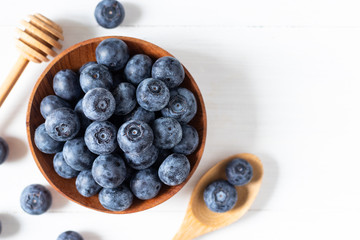 Blueberries in a wooden bowl on white table in top view or flat lay, fresh fruit