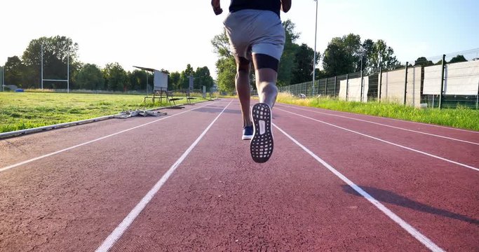 Slow motion of young african male athlete is running on race track in athletics stadium in a sunny day.