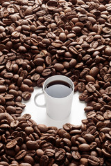A white coffee cup is in the middle of coffee beans. Concept of coffee addiction. 