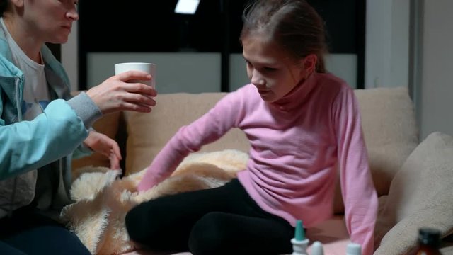 Mother gives her sick little daughter tea to drink.