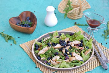 Light salad with arugula, lettuce, grilled chicken and honeysuckle on a brown plate on a turquoise background. Healthy food, diet. Selective focus
