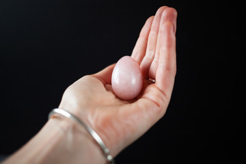 woman holding in hand a vaginal (yoni) egg. Rose quartz crystal jade egg. Copy space