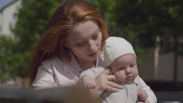 Portrait pretty young beautiful mom holding adorable baby in her arms and talking to him in a spring sunny day outdoors. Happy family.