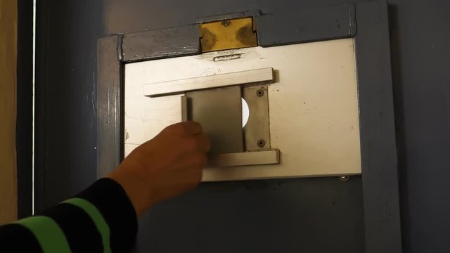 Hand opening prison cell door observation window sliding panel. Blurred view through window.