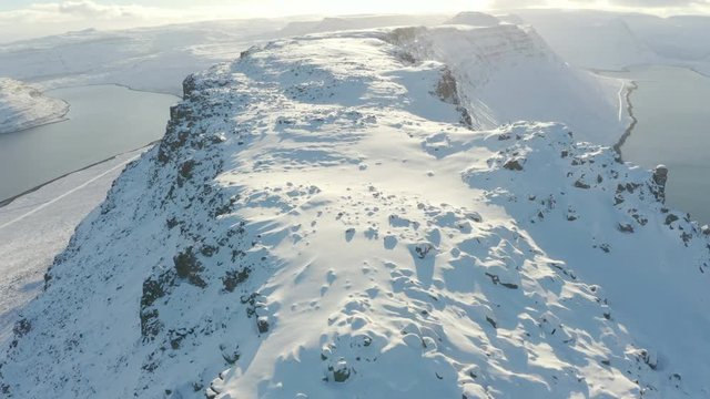 AERIAL BIRDSEYE TILT DOWN: Tracking along peak/ridge of Icelandic mountain range, deep snow jagged rocks beautiful sun set. near Isafjordur, Westfjords, Iceland, Europe