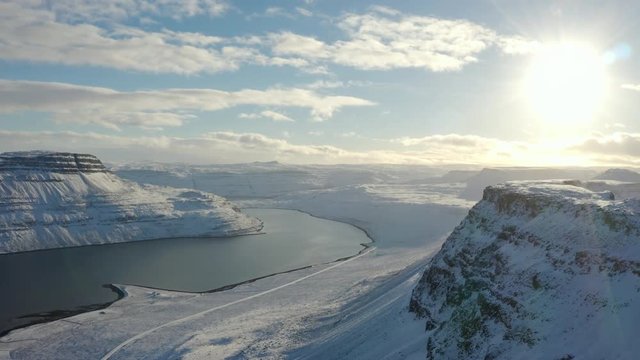 AERIAL panning Drone in Westfjords of iconic Iceland mountain ranges (fjords) towards a raging sun setting on horizon and