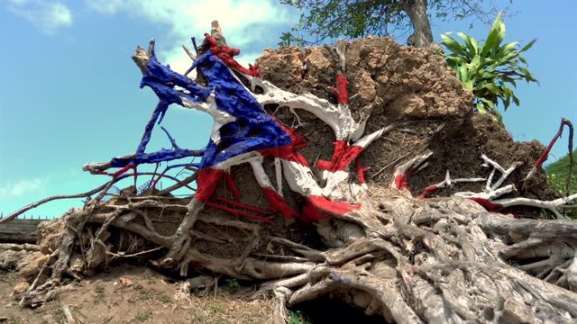 A close-up​ gimbal shot of the Puerto Rican flag painted onto an uprooted tree on a San Juan beach, its colors are vibrant in nature, on a breezy and sunny day.