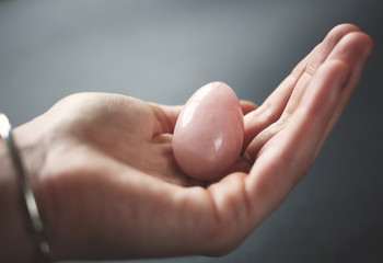 woman holding in hand a vaginal (yoni) egg. Rose quartz crystal jade egg. Copy space
