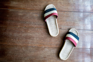 Slipper weave by handmade on wooden floor surface background. Pair of shoe on red and blue colour ready to ware at home. Concept of comfort home relax and holiday free time.