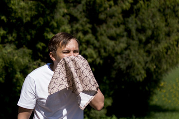 Closeup portrait of a young man with allergies. A man sneezes into a scarf on the background of...