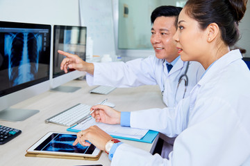 Asian male doctor pointing at computer monitor with x-ray image and discussing some problems with...