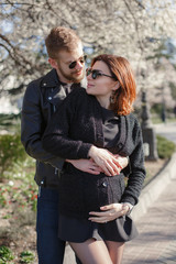 A couple in love, a man and a pregnant woman, walk together in the spring in a beautiful sunny city.Pregnant woman and man hug each other and show their love. Happy couple is expecting a baby.