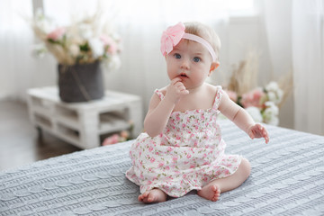 Charming beautiful lovely small female baby with plump cheeks creeps on bed, looks innocently on...