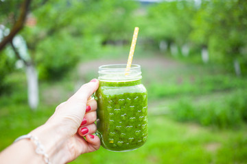 woman's hand holding jar with green cold-pressed juice, vegetable garden background. Healthy eating, detoxing, juicing, body cleancing concept