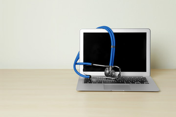 Laptop with blank screen and stethoscope on table against light background, space for text....