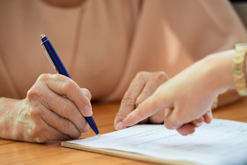 Close-up of mature woman sitting at the table putting her signature on document with pen while...