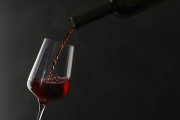Pouring red wine from bottle into glass on dark background. Space for text