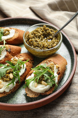 Plate with tasty bruschettas and pesto sauce on wooden table, closeup