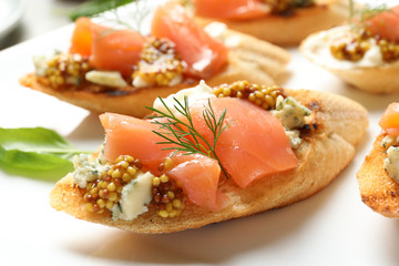 Tasty bruschettas with salmon and blue cheese on plate, closeup