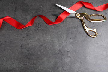 Stylish scissors and red ribbon on grey background, flat lay with space for text. Ceremonial tape...