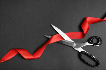 Stylish scissors and red ribbon on black background, flat lay with space for text. Ceremonial tape cutting