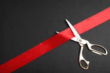 Stylish scissors and red ribbon on black background, flat lay with space for text. Ceremonial tape cutting