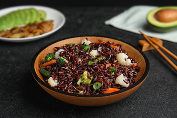 Plate of brown rice with vegetables on black table