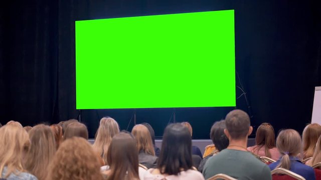 Session or debate of people in large class room. Modern cinema space for watching movies with display or monitor at background. Humanity are watching a film or a new product show on TV air events