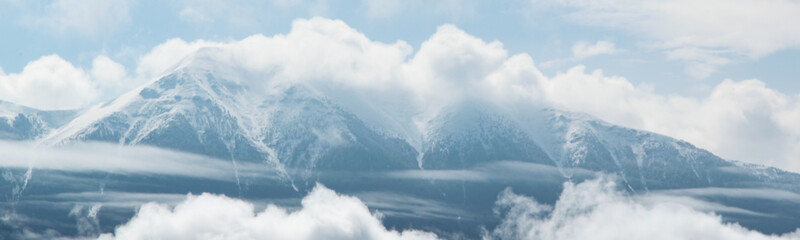 Fototapeta na wymiar Cloudy snowy Alps peaks. Foggy mountain landscape
