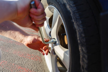 Close-up hands with cylinder wrench unscrew damaged wheel of car. Man changes flat wheel after car breaks down. Wheel balancing, repair and replacement car tires on wheels. Tire installation concept