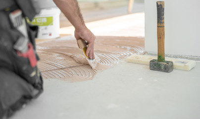 Handwerker verteilt den Parkettkleber mit der Kleberspachtel auf dem frischen Estrich beim Parkett...
