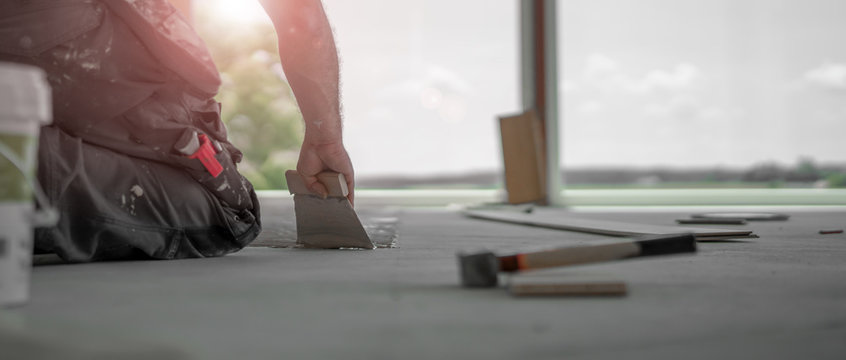 Handwerker verteilt den Parkettkleber mit der Kleberspachtel auf dem frischen Estrich beim Parkett legen
