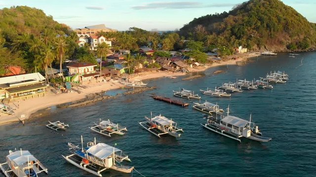 Aerial drone parallax shot of a bay with docked fishing boats and small houses and huts on the coast of Apo island the Philippines