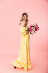 Young blonde woman posing isolated over pink wall background holding flowers