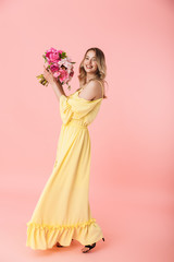 Young blonde woman posing isolated over pink wall background holding flowers