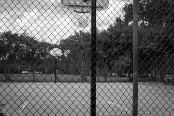 Grey toned basketball court from behind fence - obrazy, fototapety, plakaty