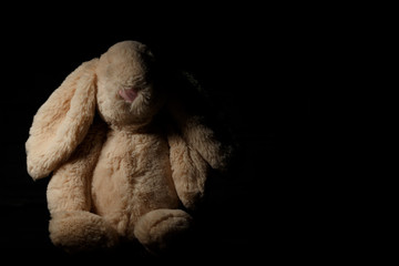 Soft toy  rabbit on a dirty dark background in the beam of hard light with shadow. Lost childhood...