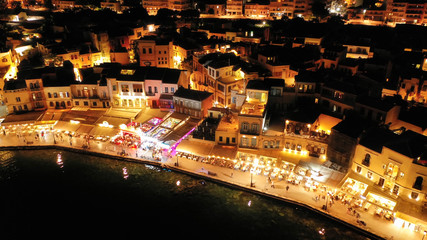 Aerial drone night shot of iconic and picturesque illuminated Venetian old port of Chania with famous landmark lighthouse and shops - restaurants serving Cretan traditional food, Crete island, Greece