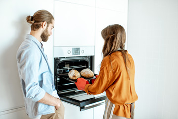 Fototapeta premium Young and cheerful couple baking breads at the modern white kitchen at home